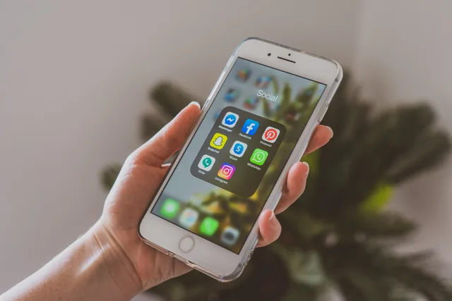 Close-up of a hand holding a smartphone displaying popular social media apps. Social listening skills as tasks to cover, not jobs to predict