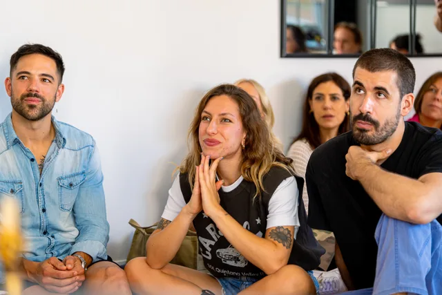A group of adults attentively listening indoors, appearing engaged and smiling, creating a warm social scene. Three social listening suppliers on the same criteria, with a method and no winner