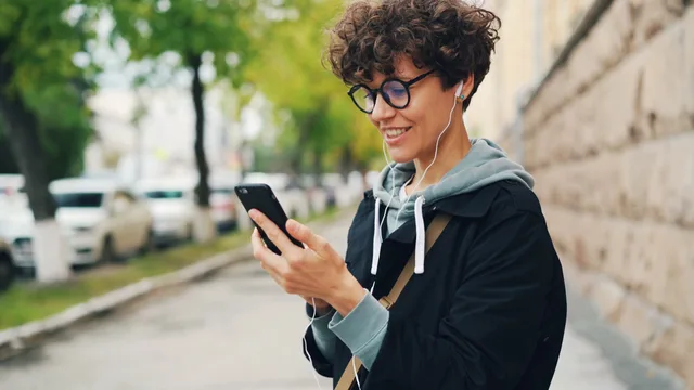 Young person enjoying music on smartphone outdoors, smiling. Social listening rules and ethics: keeping checks in their proper lanes