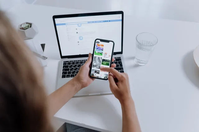 Person using both a smartphone and laptop, multitasking at a modern desk with office plants. What is social media crisis monitoring and why do UK brands need it?